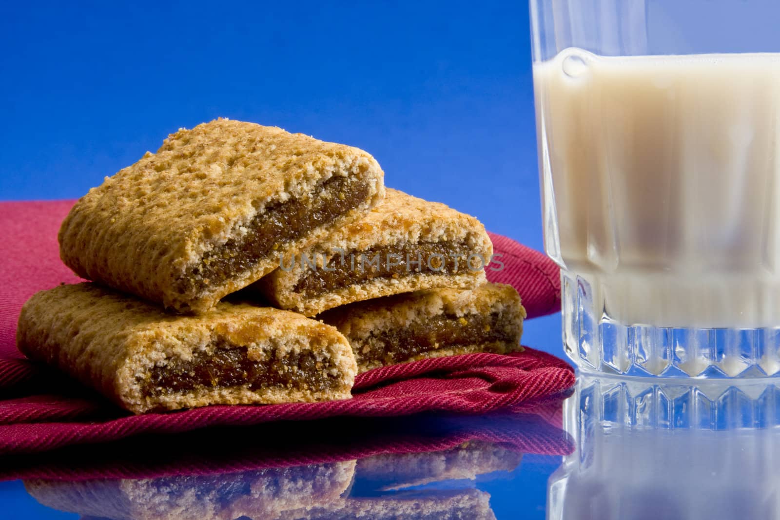 Wheat fig bars on red cloth napkin with glass of milk on blue background