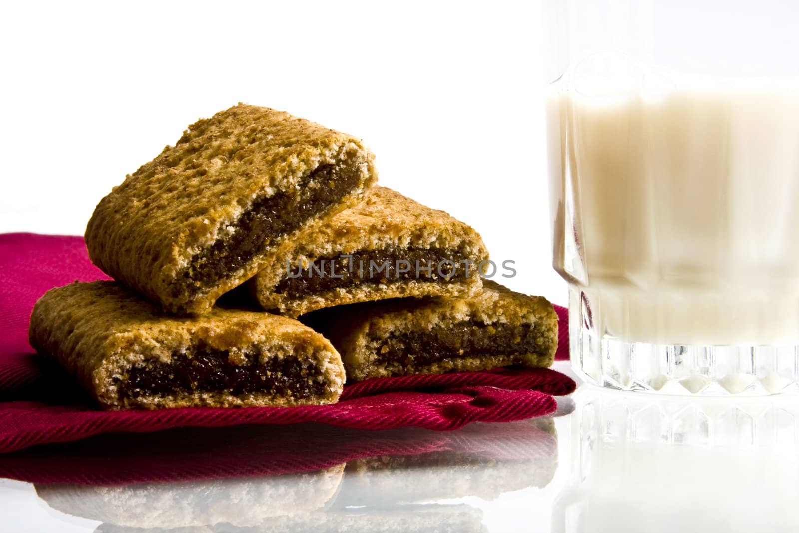 Wheat fig bars on red cloth napkin with glass of milk on white background