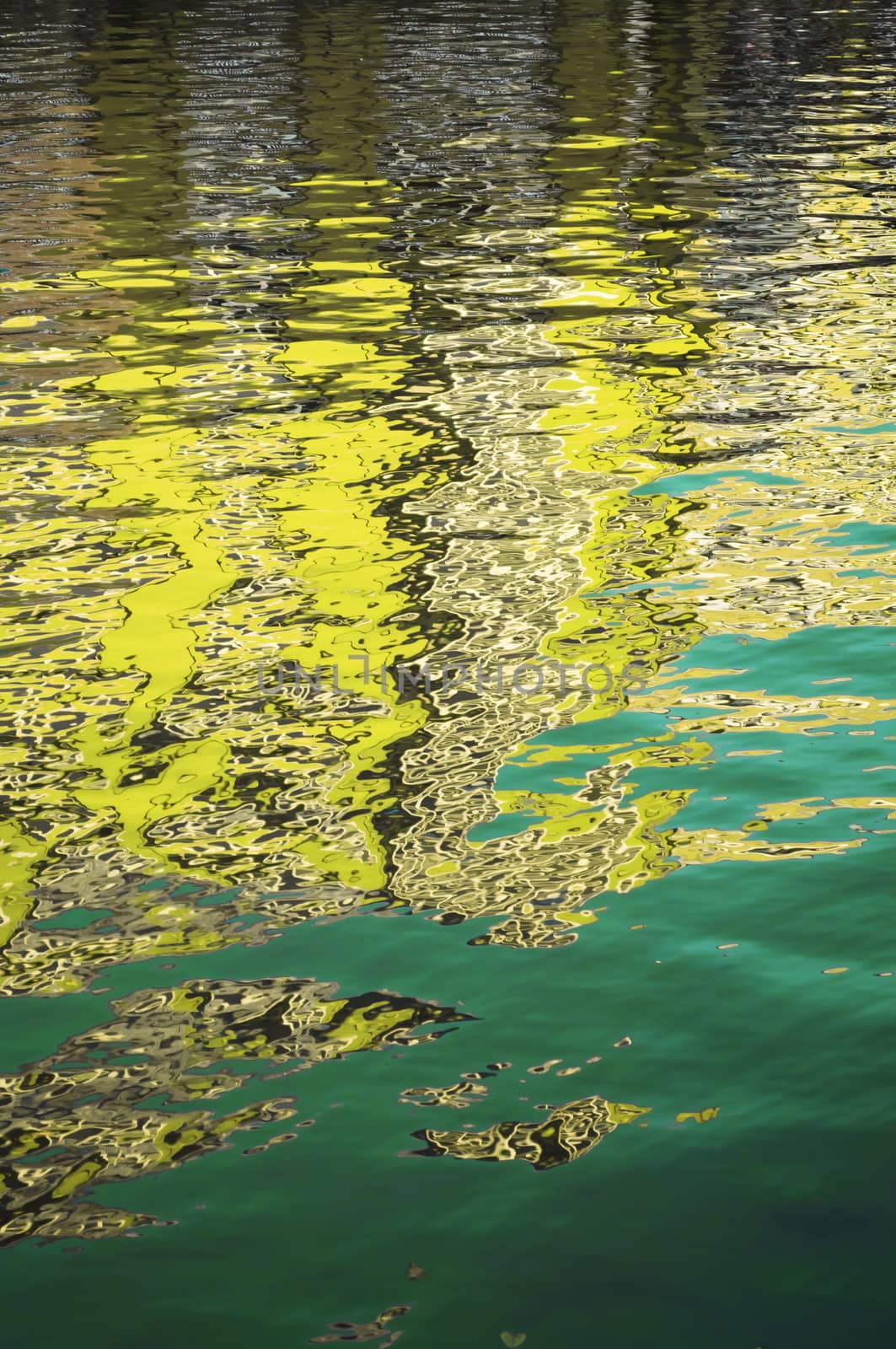 A gently rippled surface on a body of water reflecting yellow and green colours