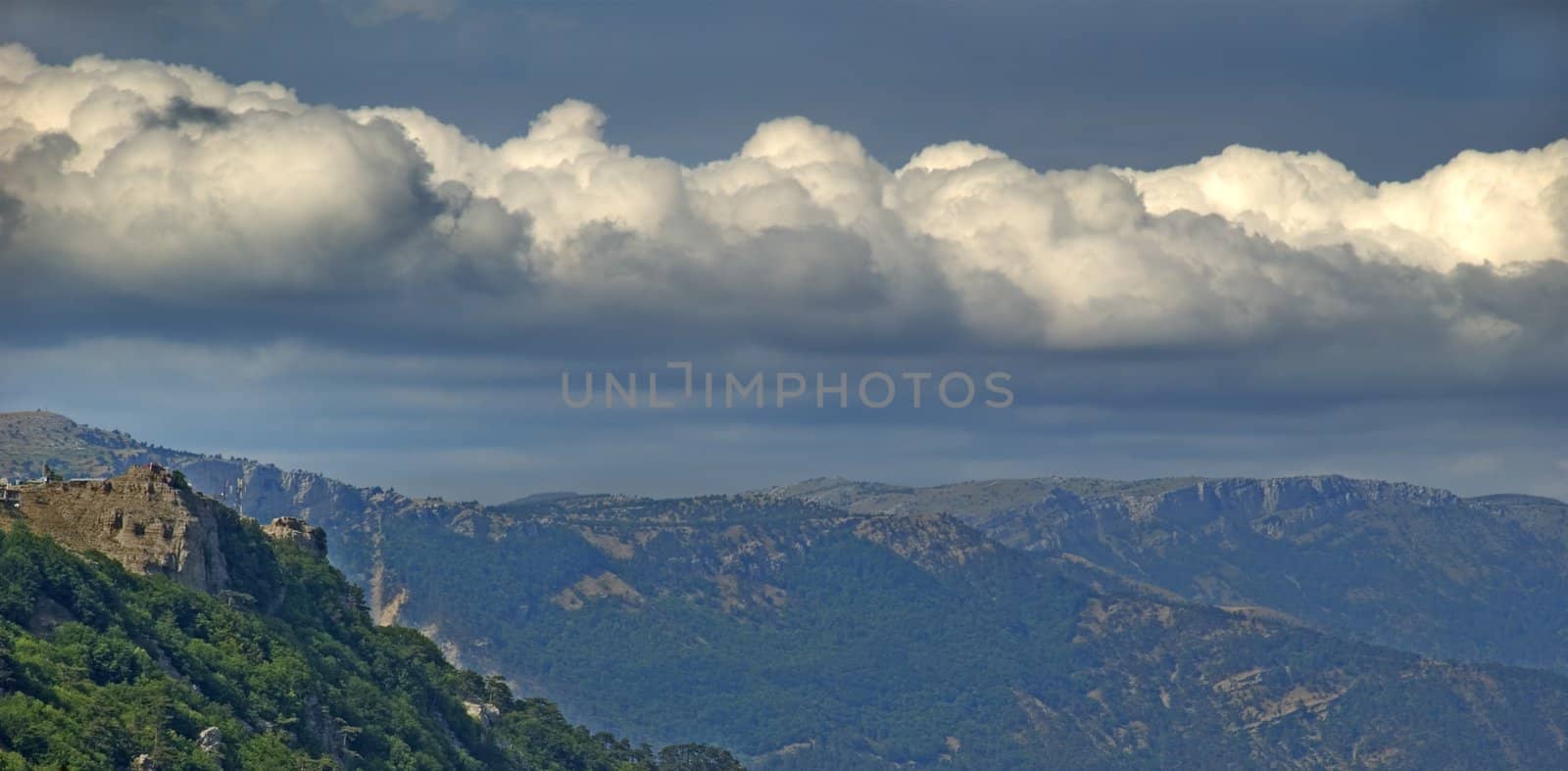 The clouds and mountains. Gleams of the sun through dense overcast above mountains