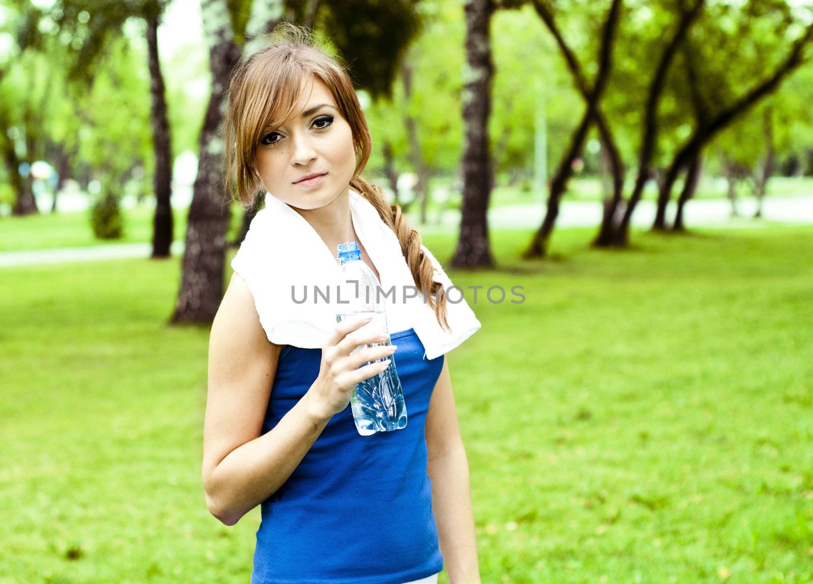 Young woman drinking water after exercise, summer park background