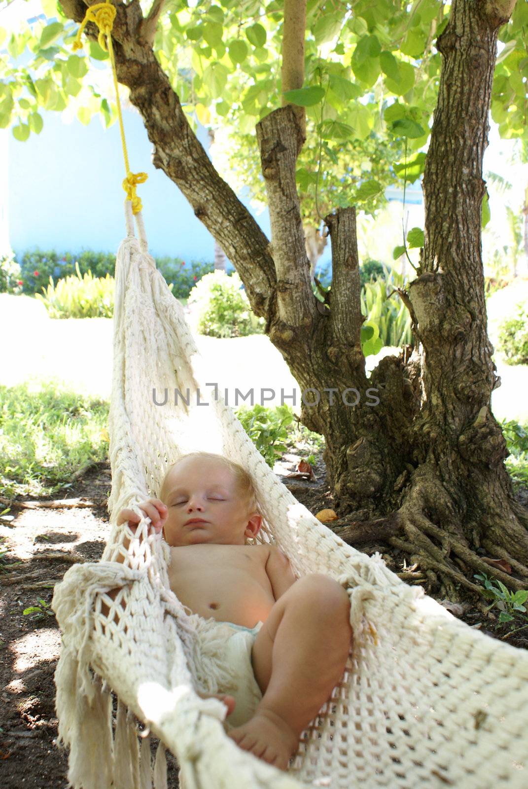 An adorable baby boy sleeps outside in a hammock while dreaming sweetly.
