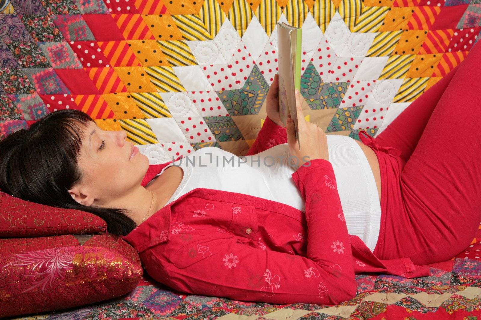expectant mother lies, smiles and reads book