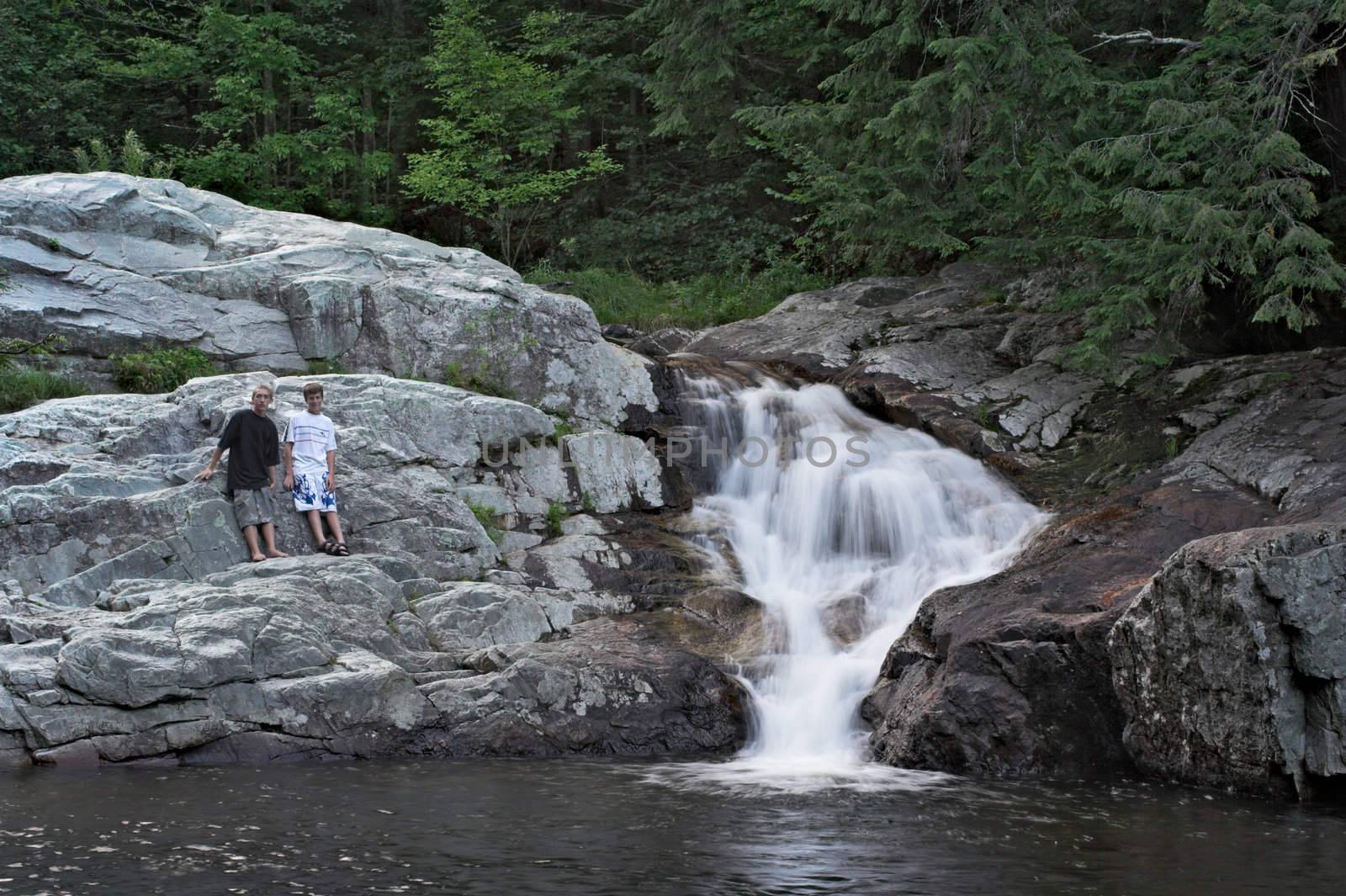 A waterfall with two boys standing on surrounding rocks