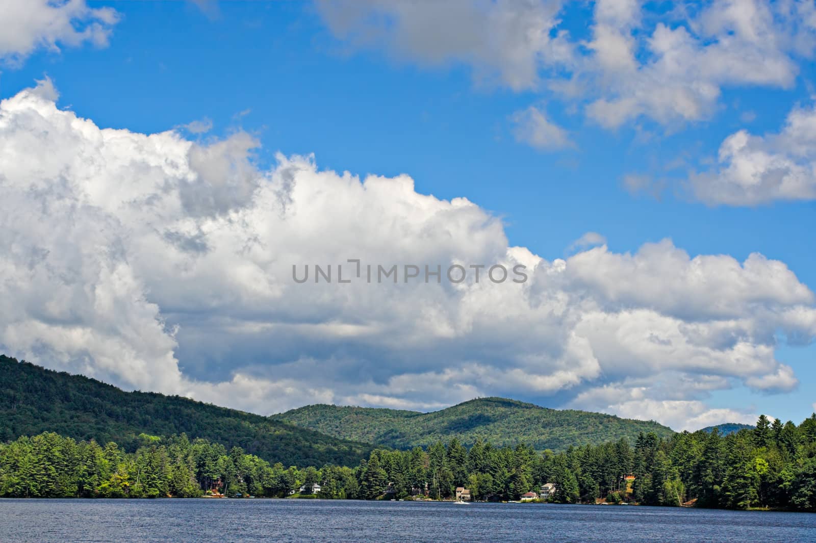 Mountains at the shoreline of a lake with large cumulus clouds in the sky above.