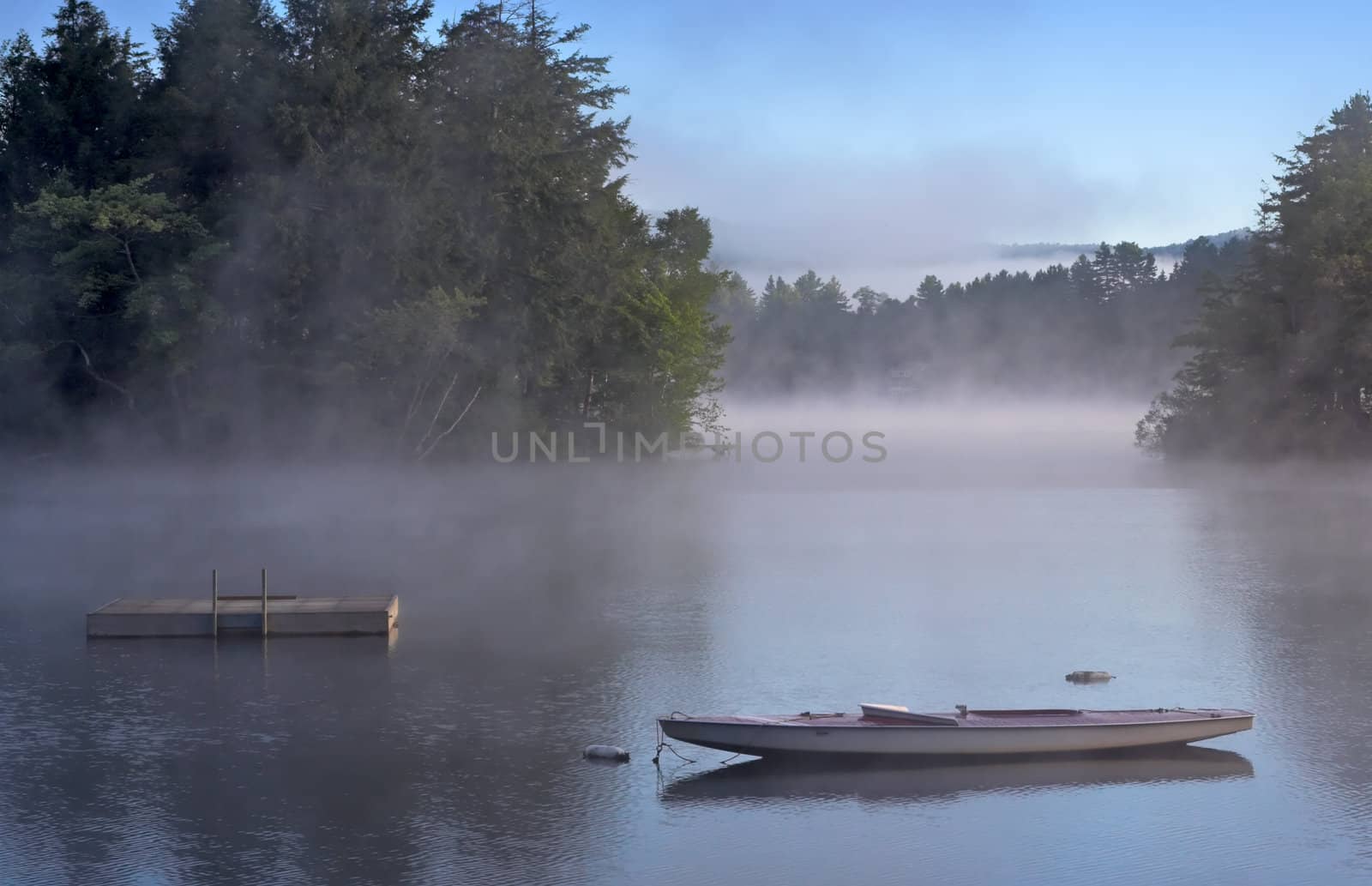 Early morning fog on a lake. A boat and dock are in the foreground.