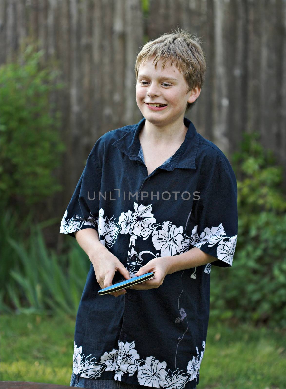 A young boy smiling while playing table tennis outside. 