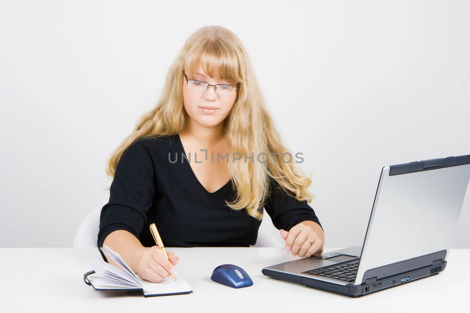 blonde girl with a laptop writes in a notebook
