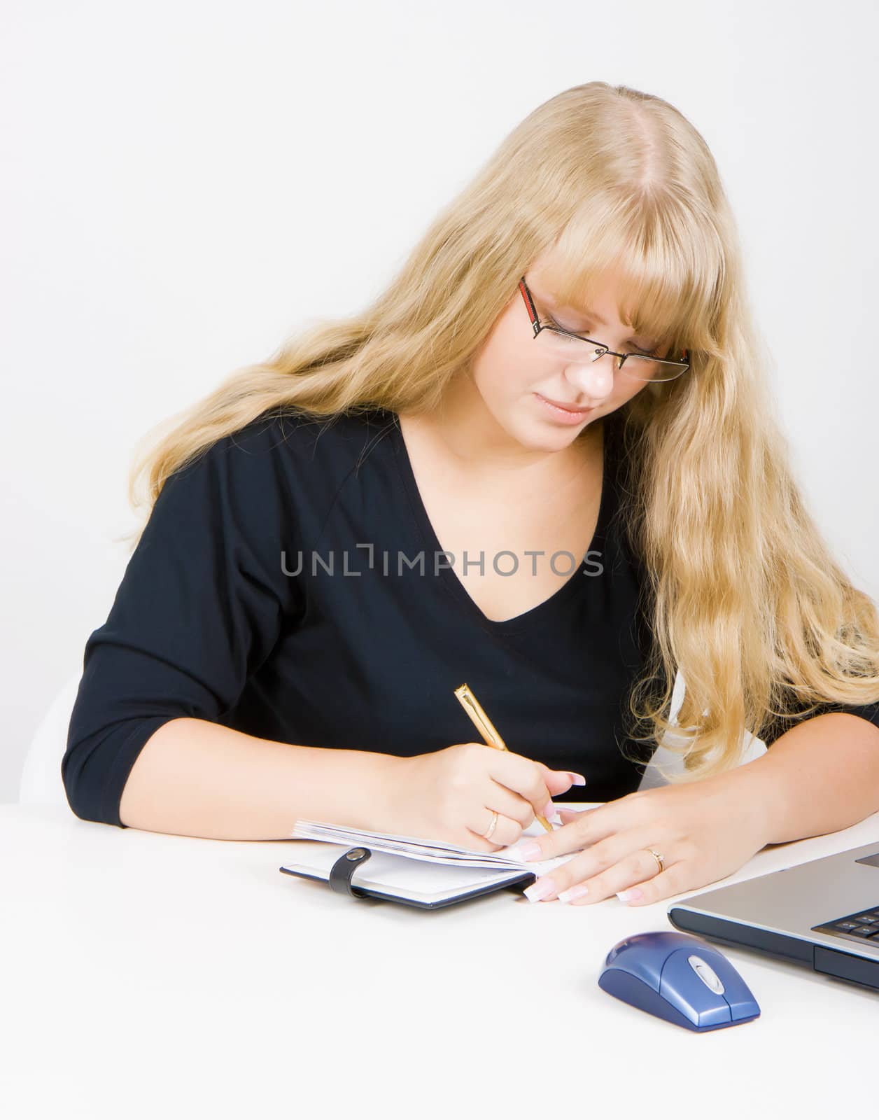 blonde girl with a laptop writes in a notebook