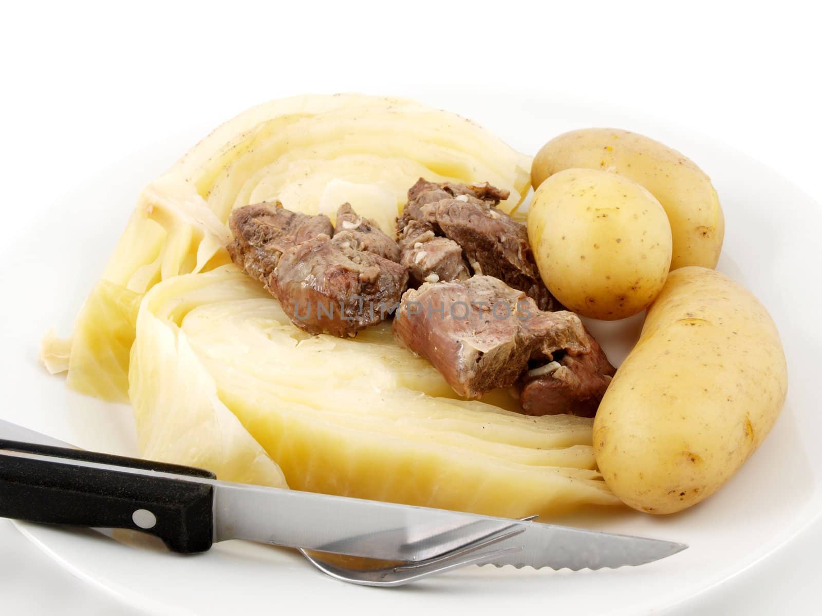 Boiled meat and cabbage, with potatoes, knife and fork, white plate towards white background