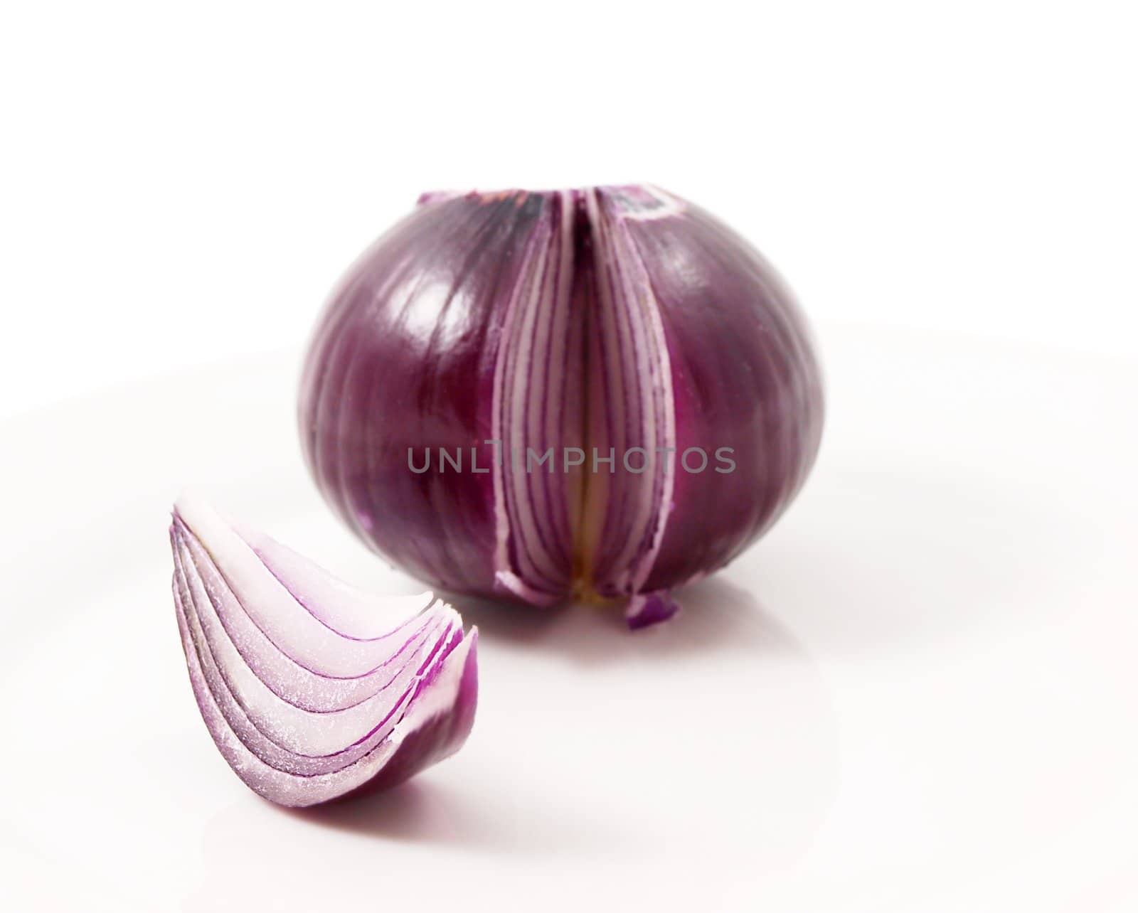 Red onion, whole, one slice up front in focus, towards white background