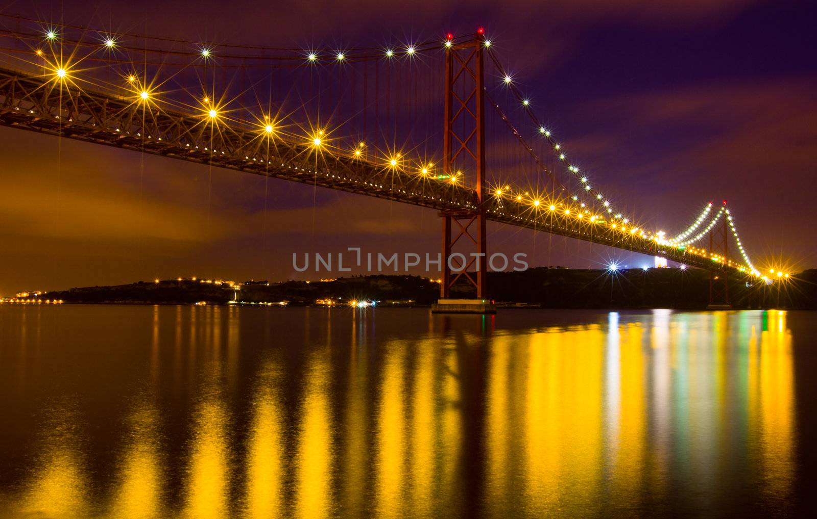 The 25 de Abril Bridge - suspension bridge over the river Tagus illuminated at night. Lisbon Portugal