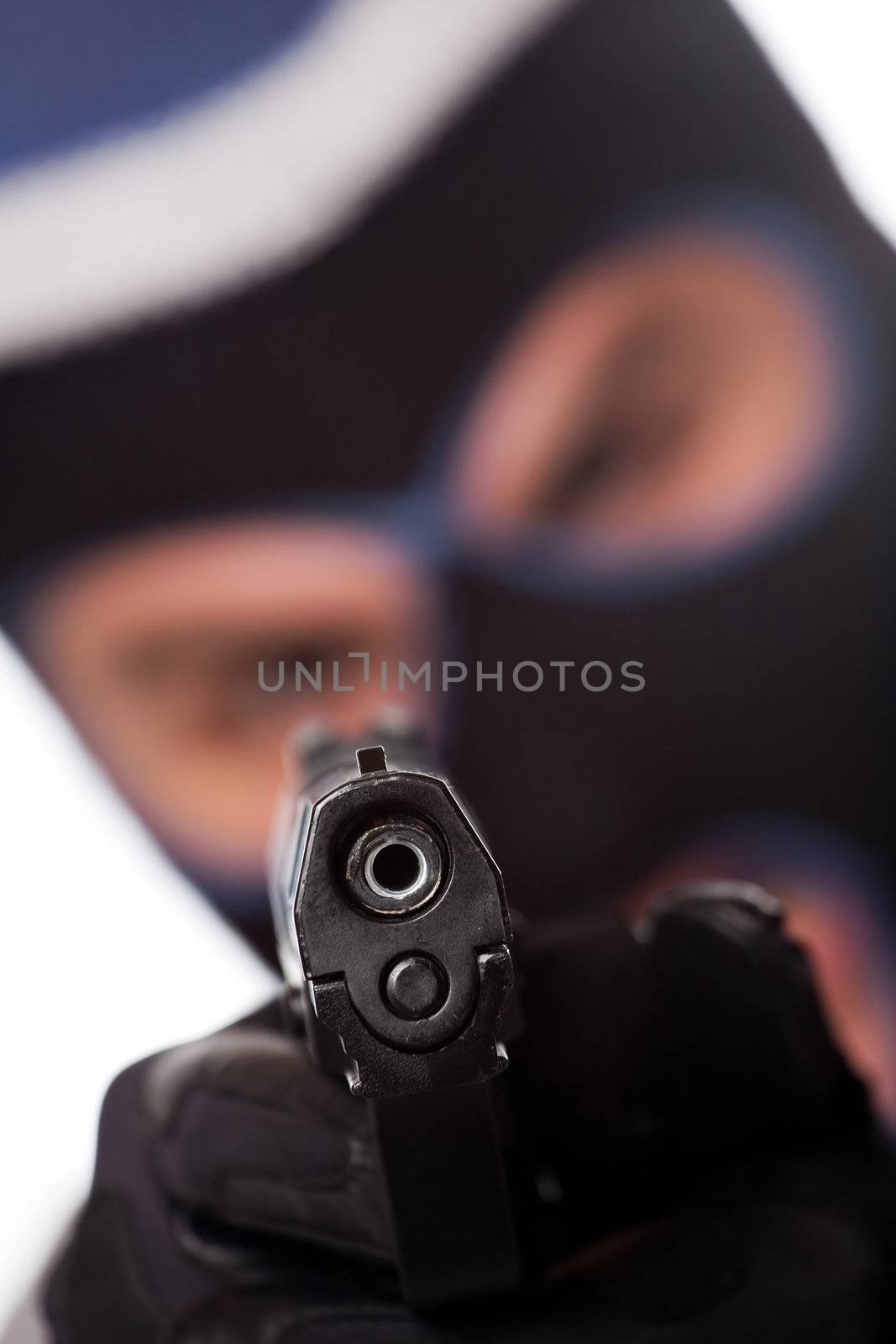 An angry looking man wearing a ski mask pointing a black handgun at the viewer. Shallow depth of field.