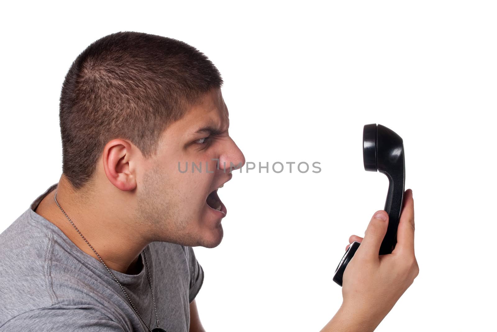 An angry and irritated young man yells into the telephone receiver over a white background.