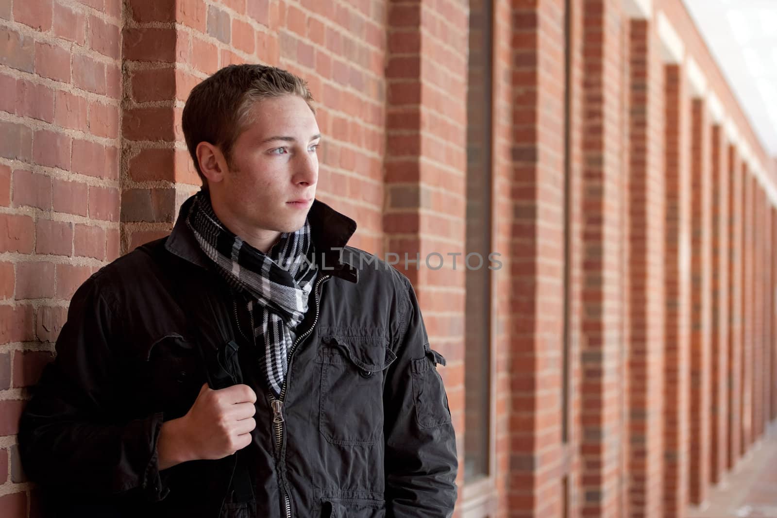 A portrait of a young man standing in an outdoor corridor with his backpack.