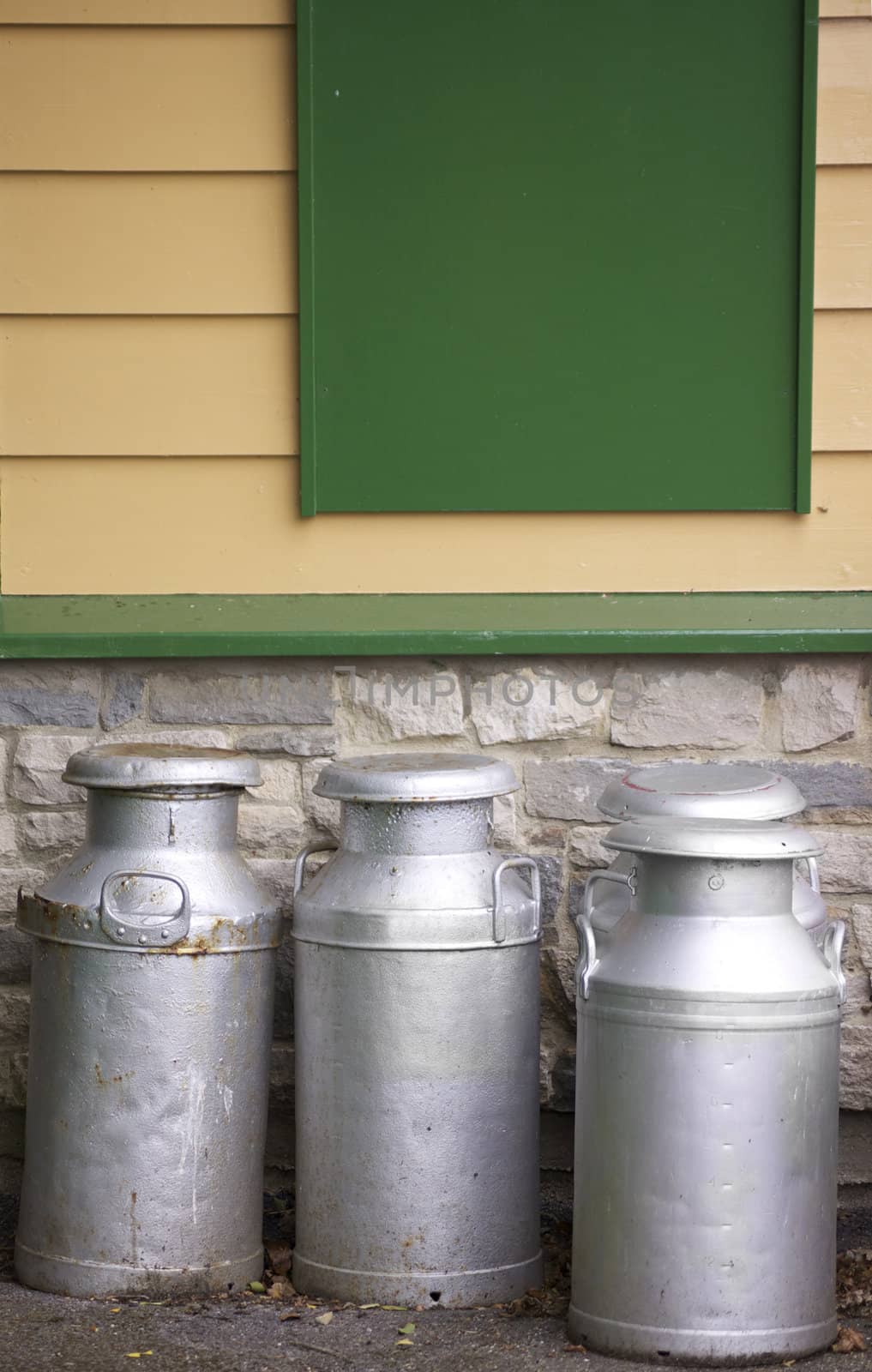 Four old tin and aluminium milk churns set in front of a wooden clad building. Located in an old railway platform in Devon, England. Part of the historical Swanage Railway system.
