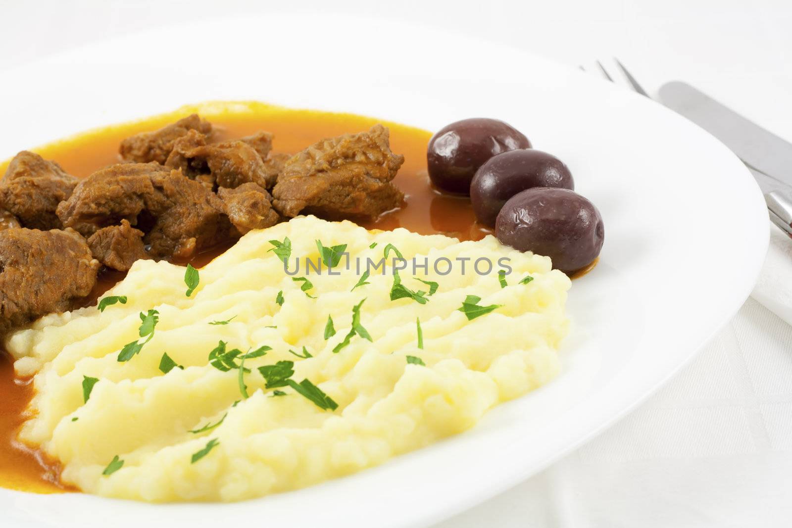 Goulash with mashed potato spiced with parsley and three brown olives.