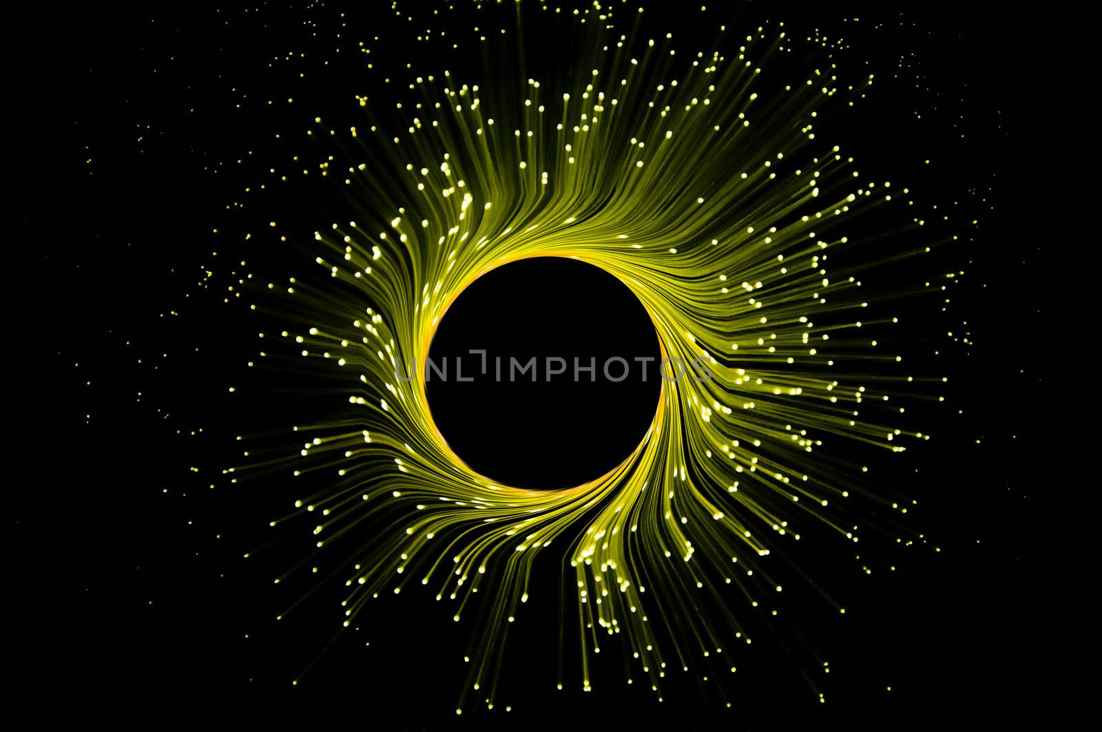 Many illuminated yellow fiber optic light strands in ring formation against black background