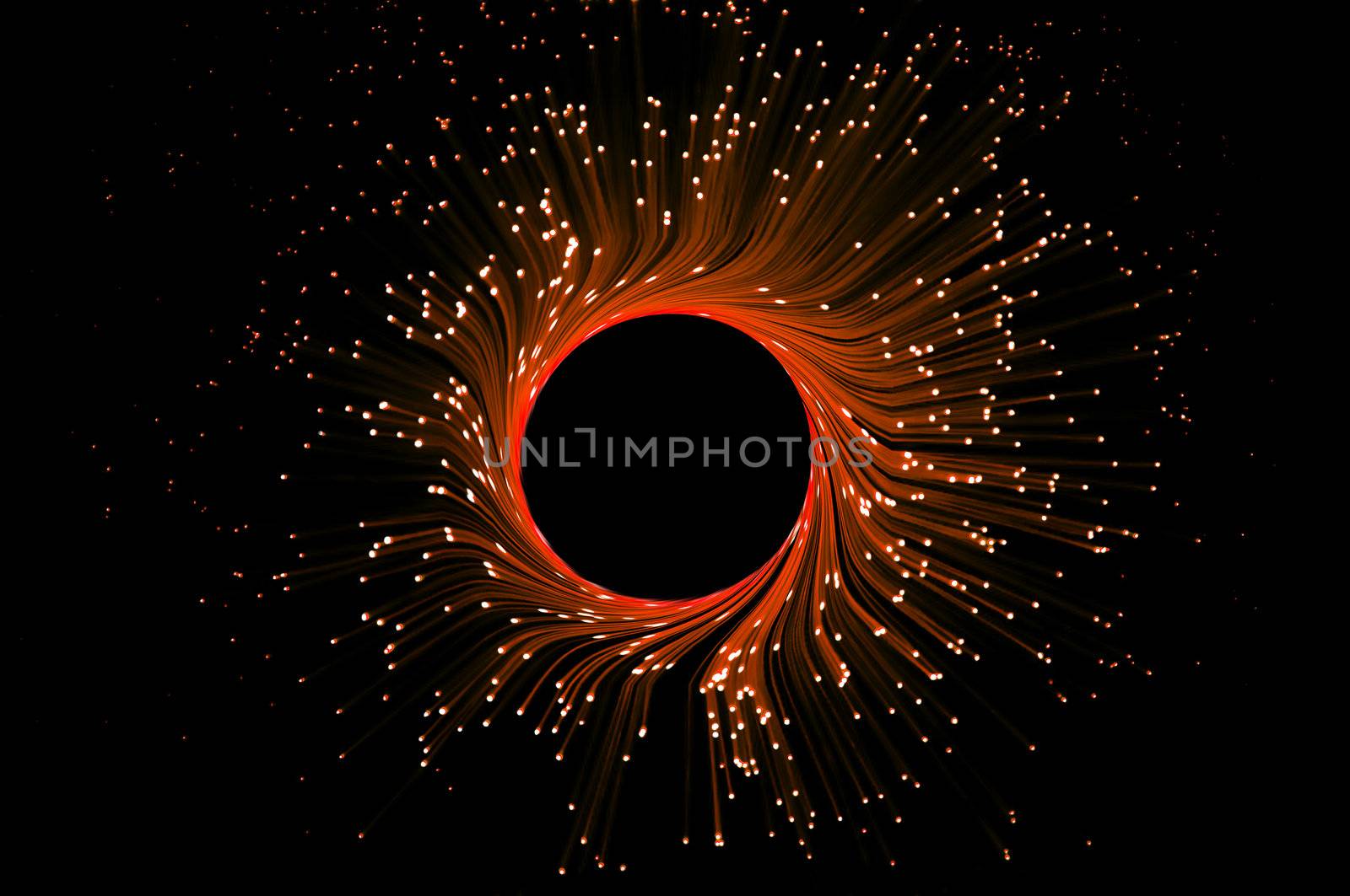 Many illuminated red and orange fiber optic light strands in a ring formation against black.