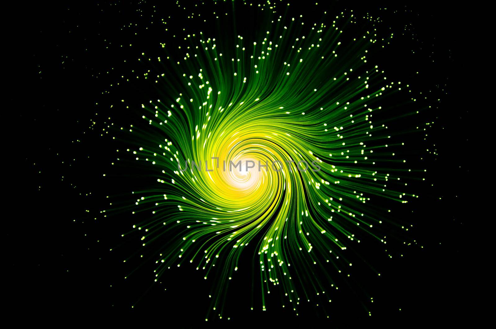 Many illuminated green and yellow fiber optic light strands swirling towards the centre against a black background.