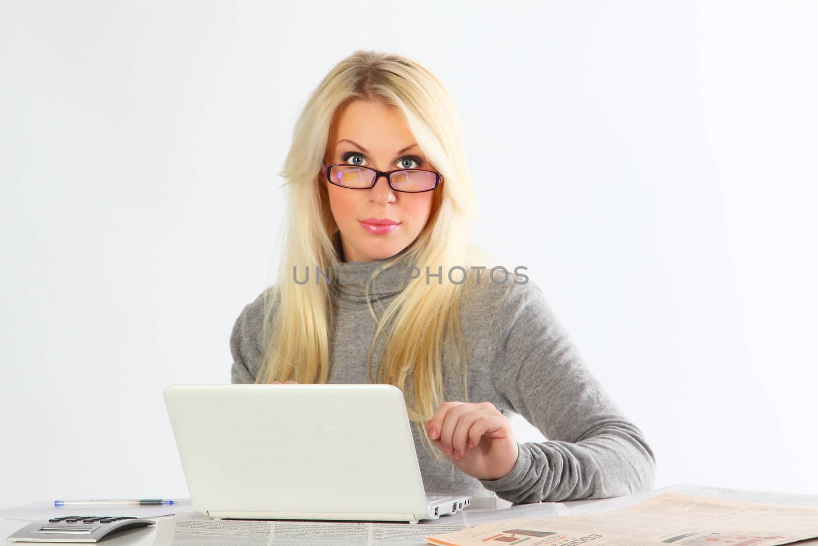 The business woman wearing spectacles with newspapers and the laptop works behind a table
