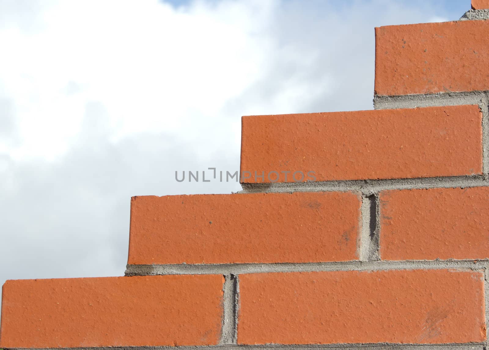 Red bricks constructed into a wall with cement pointing and a stepped jagged edge against a cloudy sky.