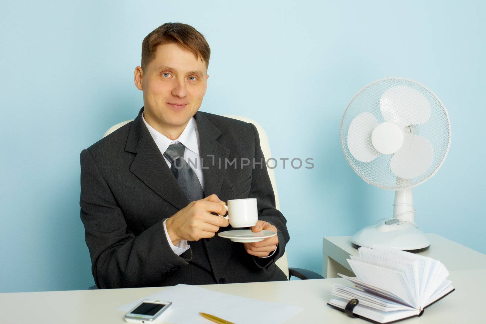 Attractive smiling young man with a cup of coffee in the office
