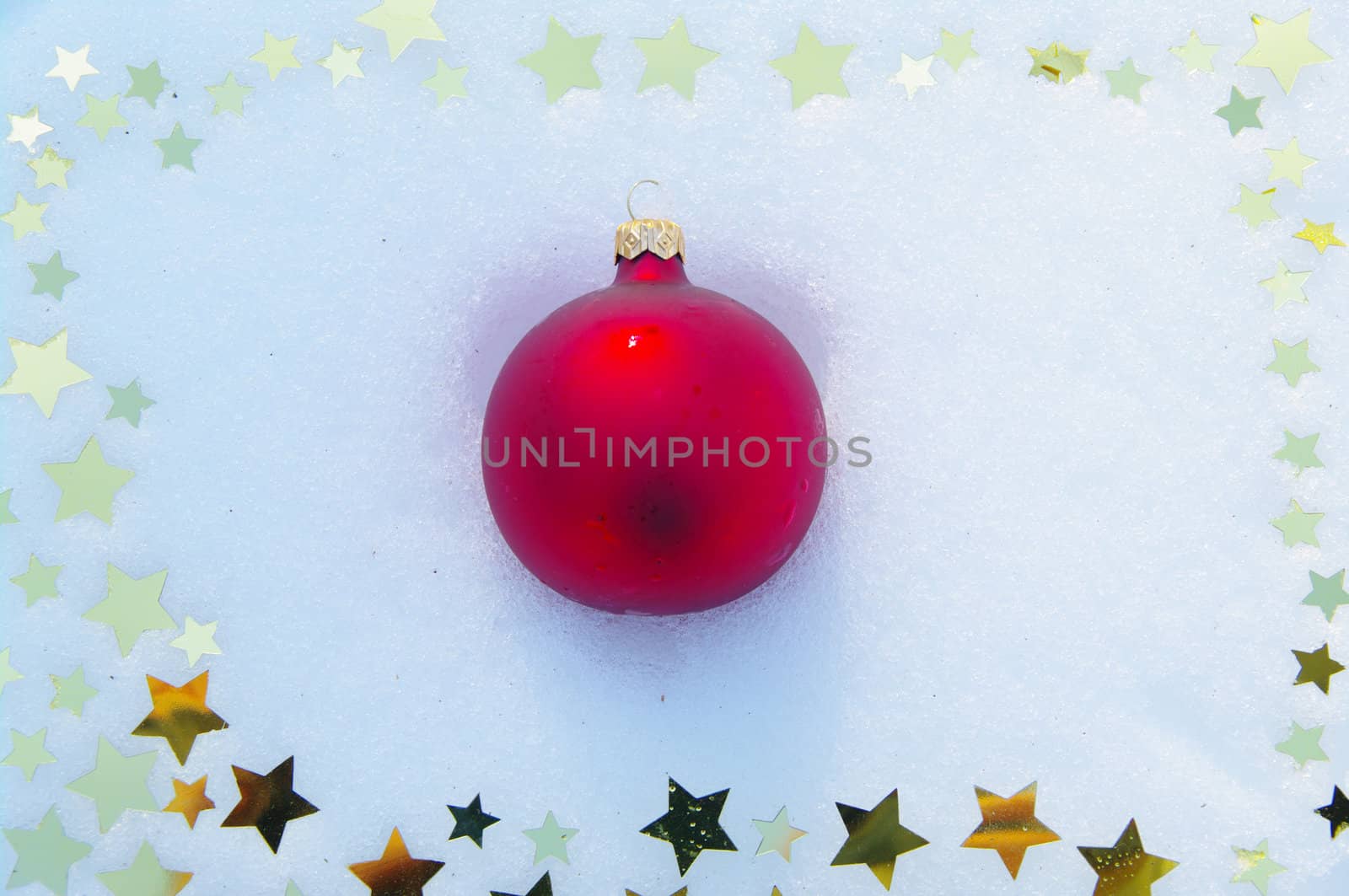 red bauble and golden snow stars on a real snowy icy surface