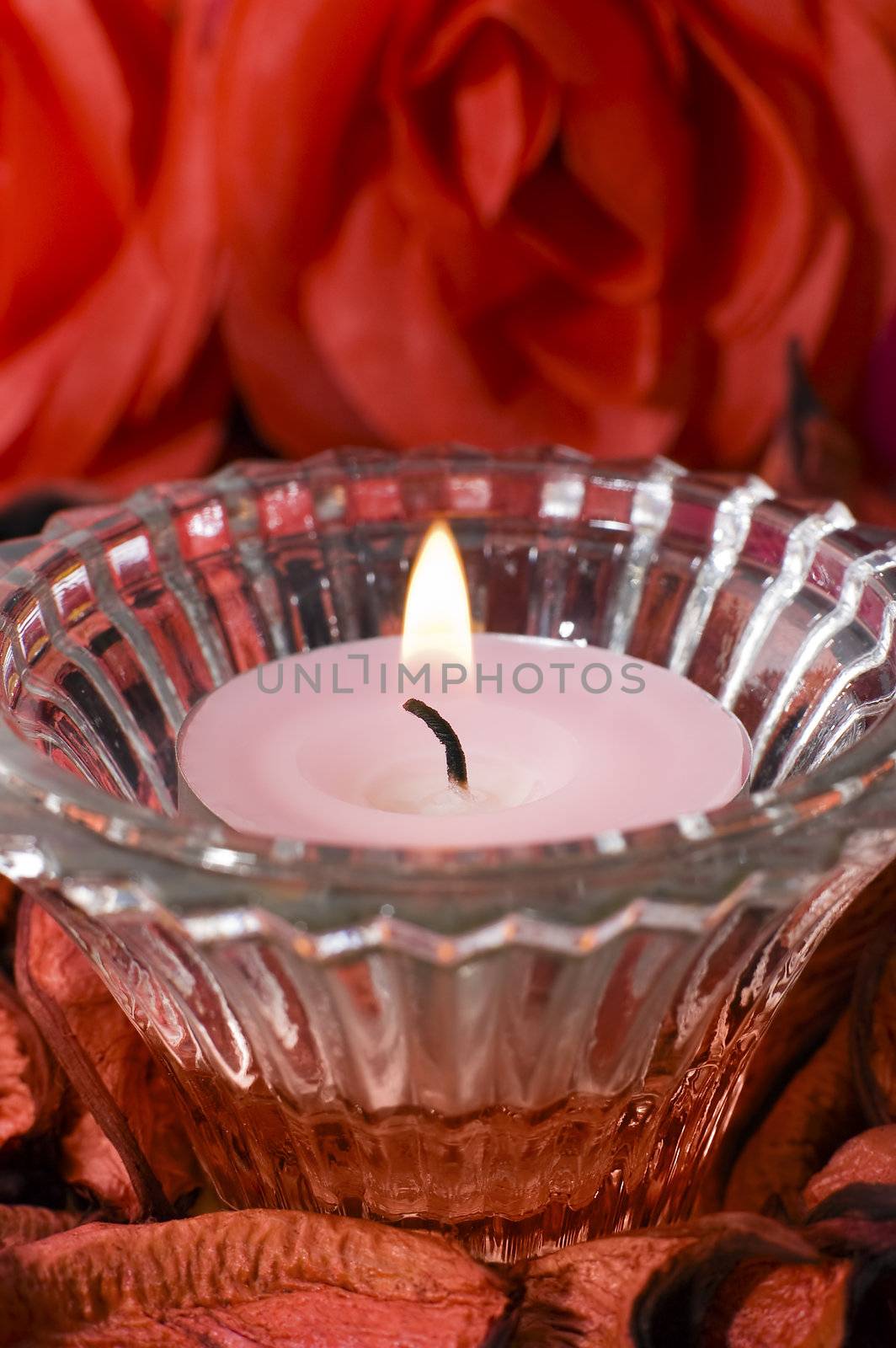 pink candle in a small decoration glass, red flower background, vertical photo