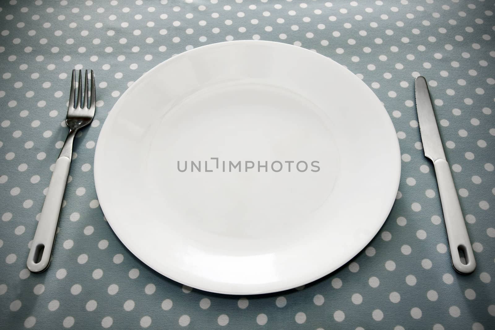 Empty white dinner plate with ustensils on fun grey polka dot tablecloth.