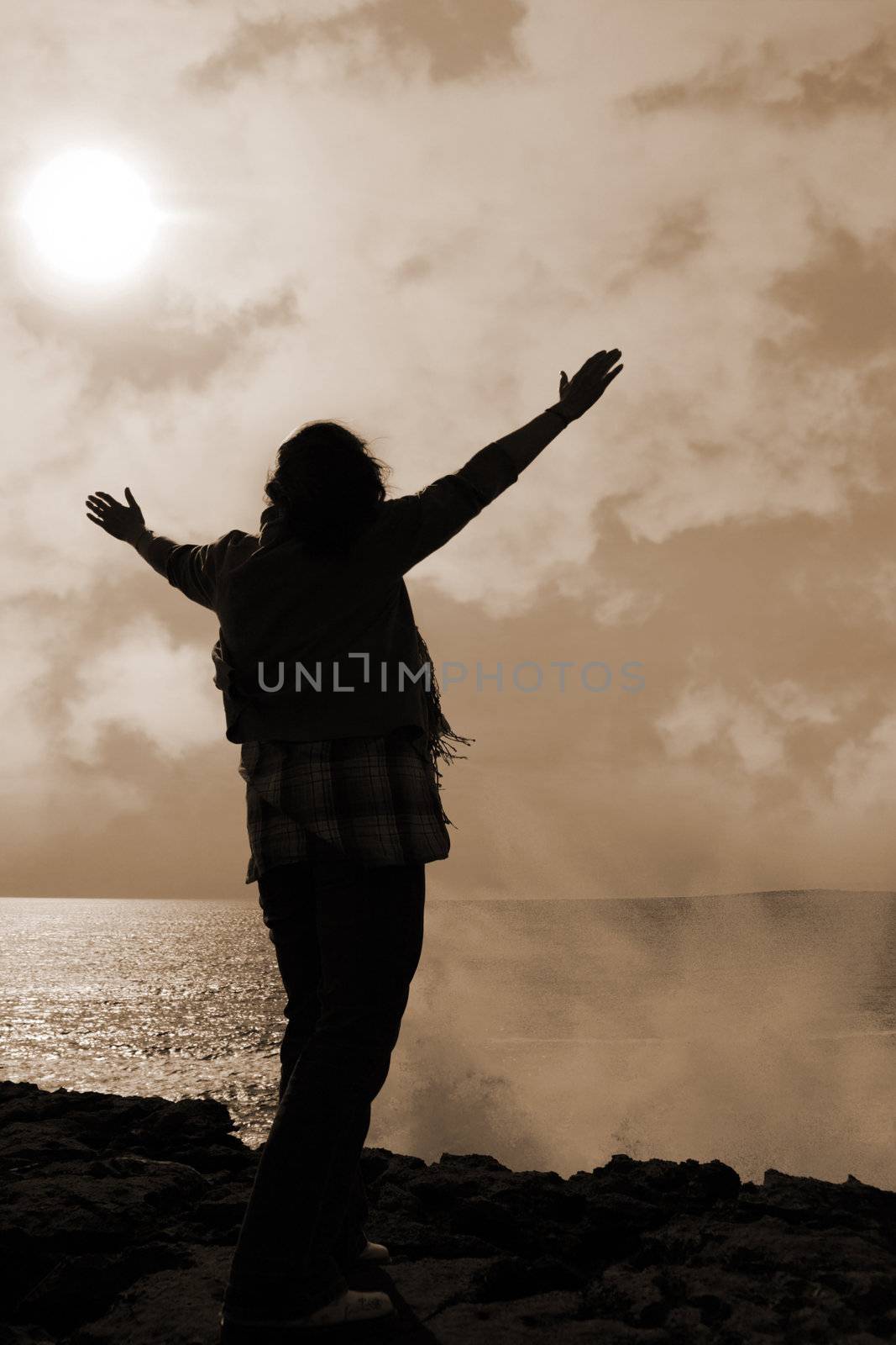 a lone woman raising her arms in awe at the powerful waves on the cliffs edge in county clare ireland in sepia