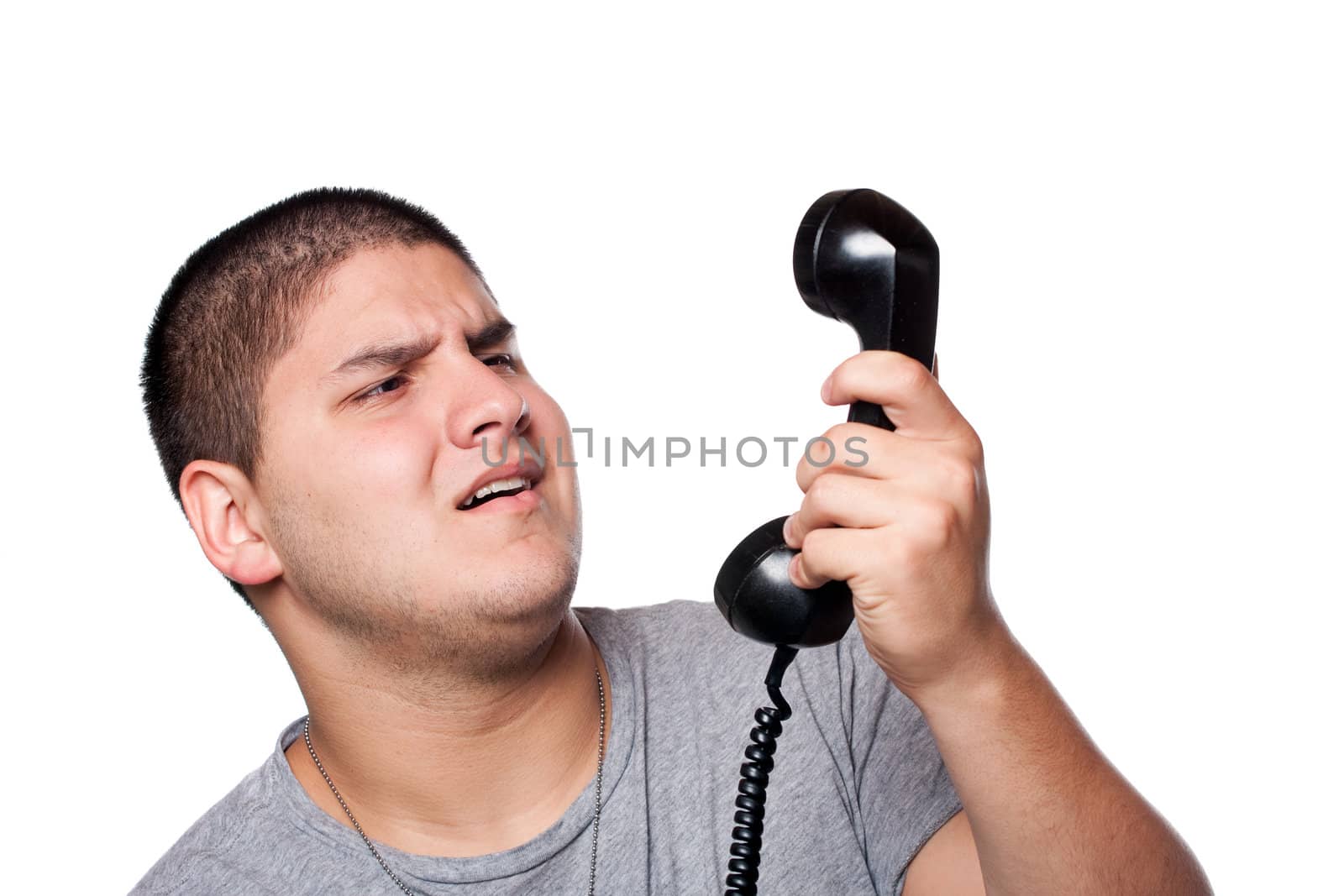 An angry and irritated young man yells into the telephone receiver over a white background.