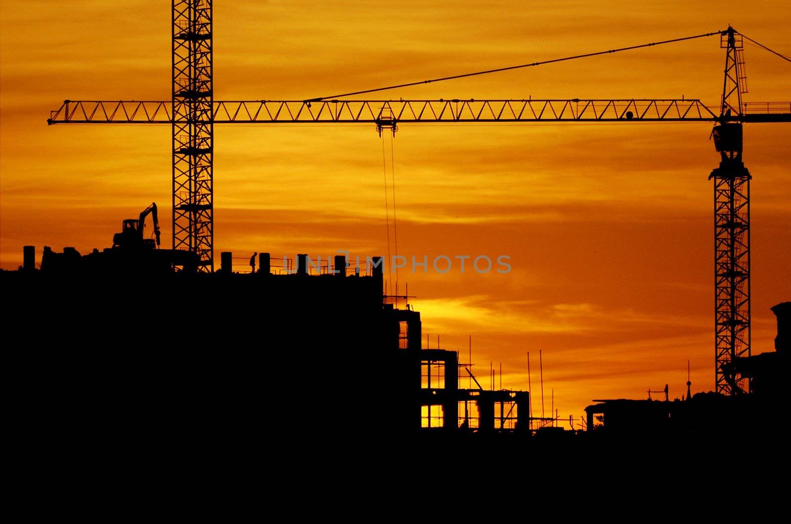 construction of a building, cranes and other machinery as silhouettes against a background of red sunset sky