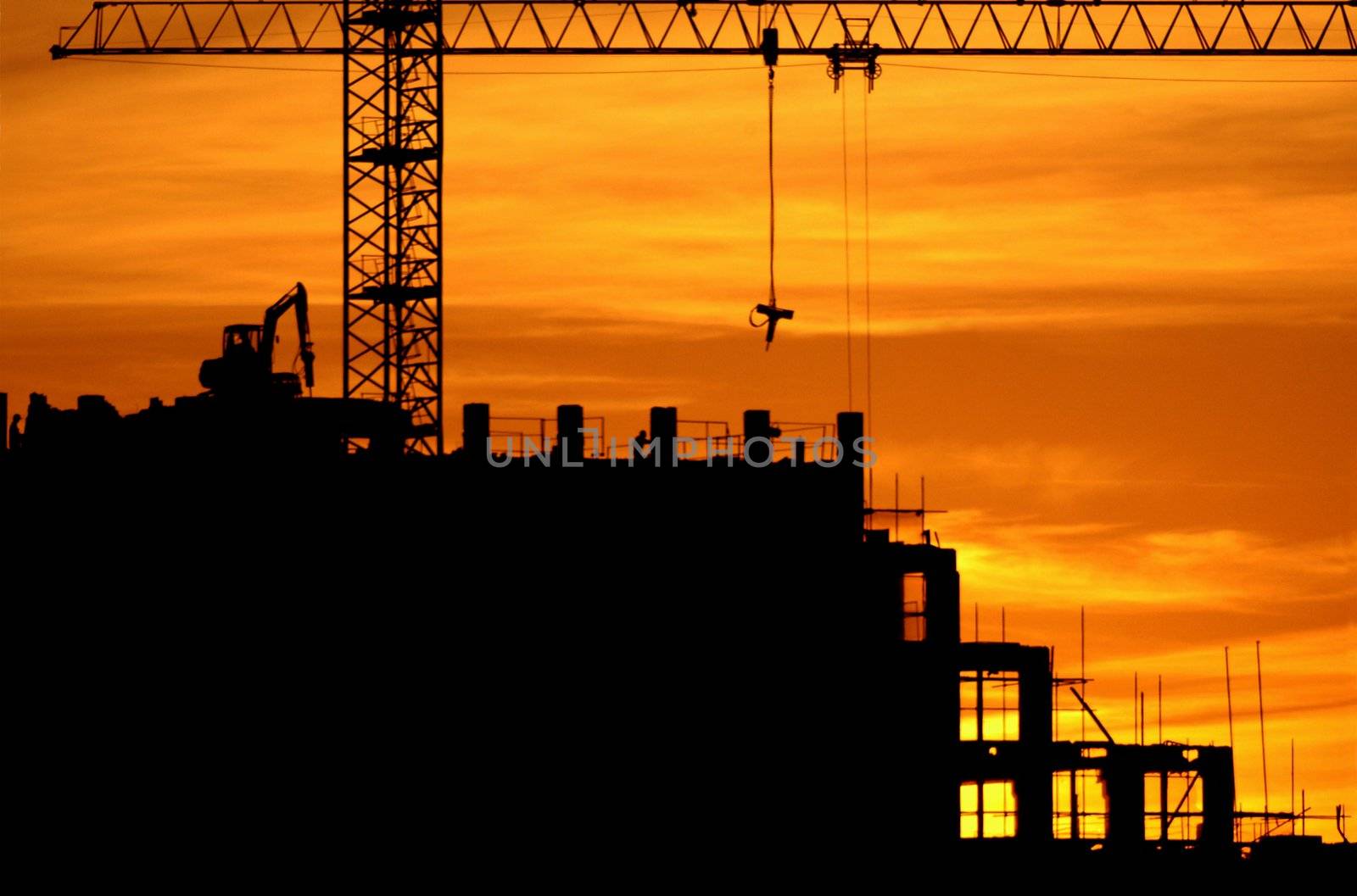 construction of a building, cranes and other machinery as silhouettes against a background of red sunset sky