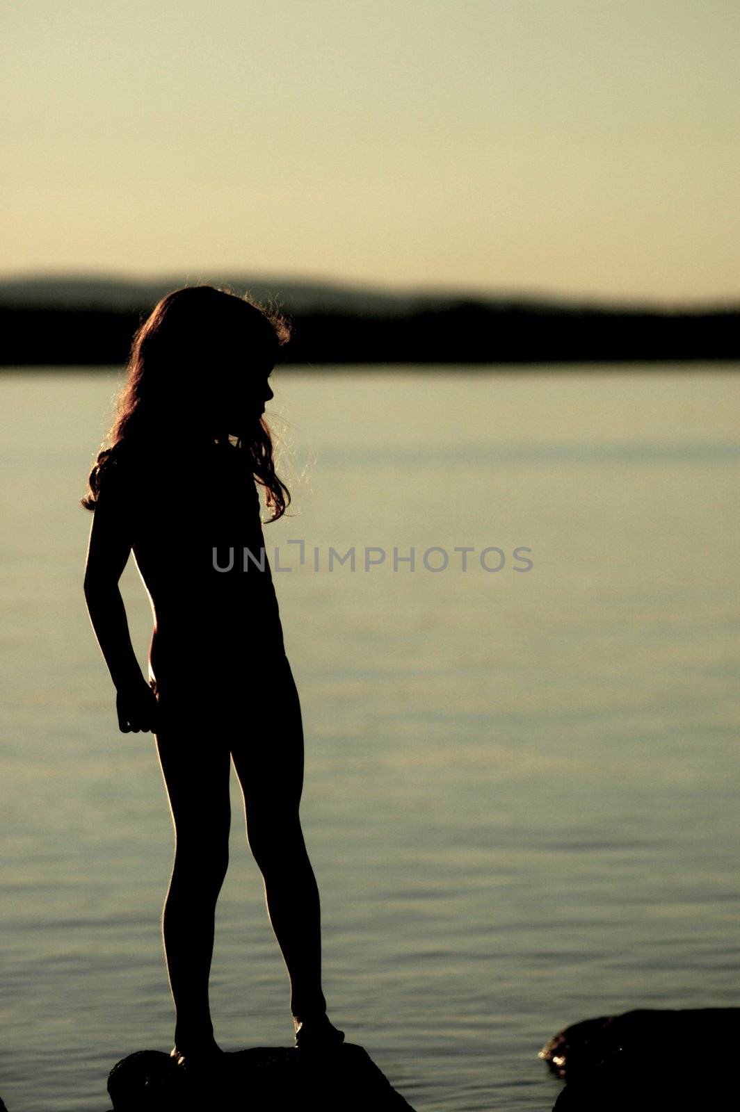 A young girl's silhouette by lake Millinocket in maine, with twilight behind her.