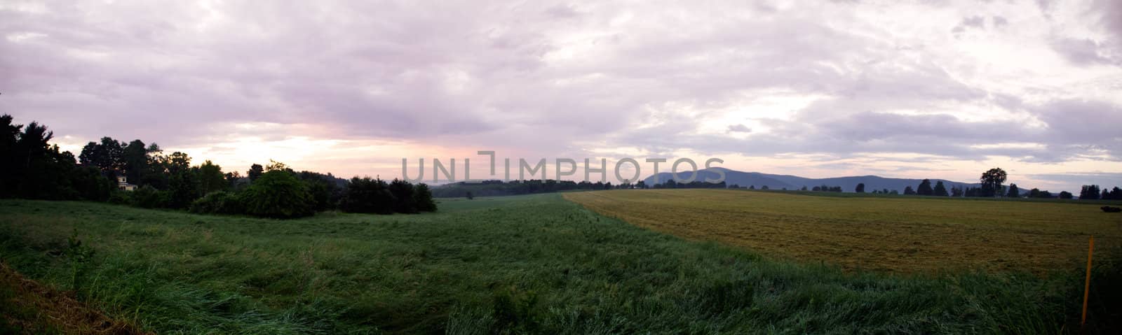 A panorama of a hill in the country in Berkshire County, Mass, U.S.  Corn fields and grass meadows meet pine trees and mountains.