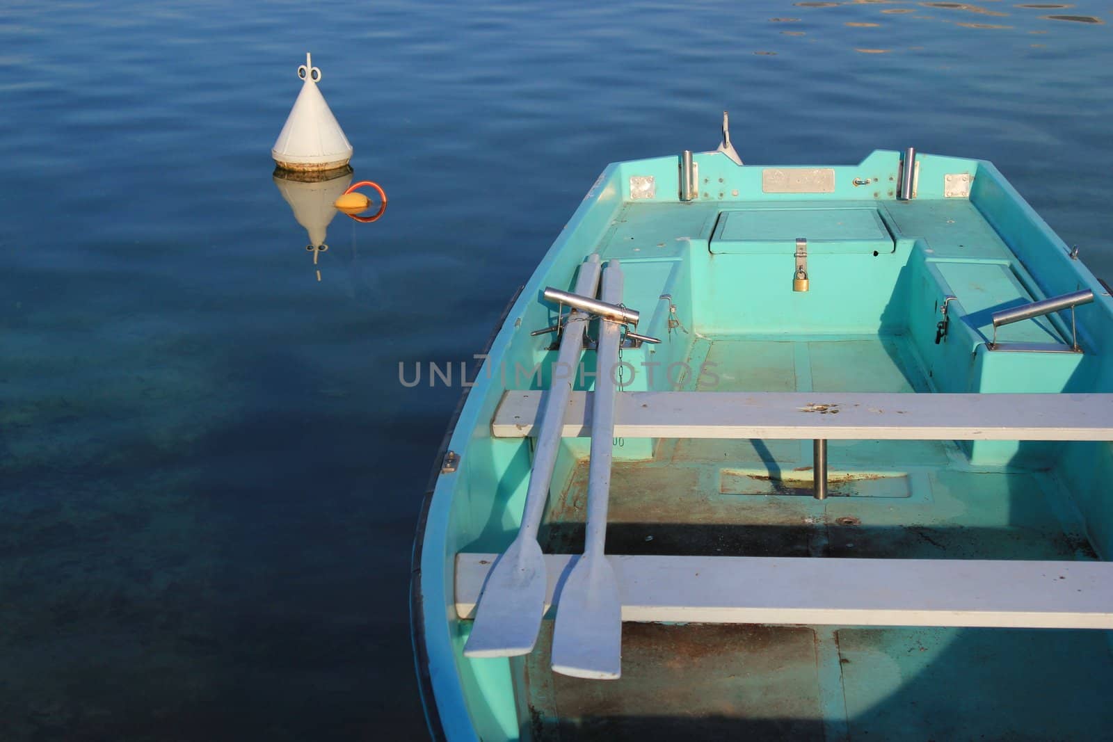 Small green boat with two paddles in it near a buoy in the waterlake of Annecy, France