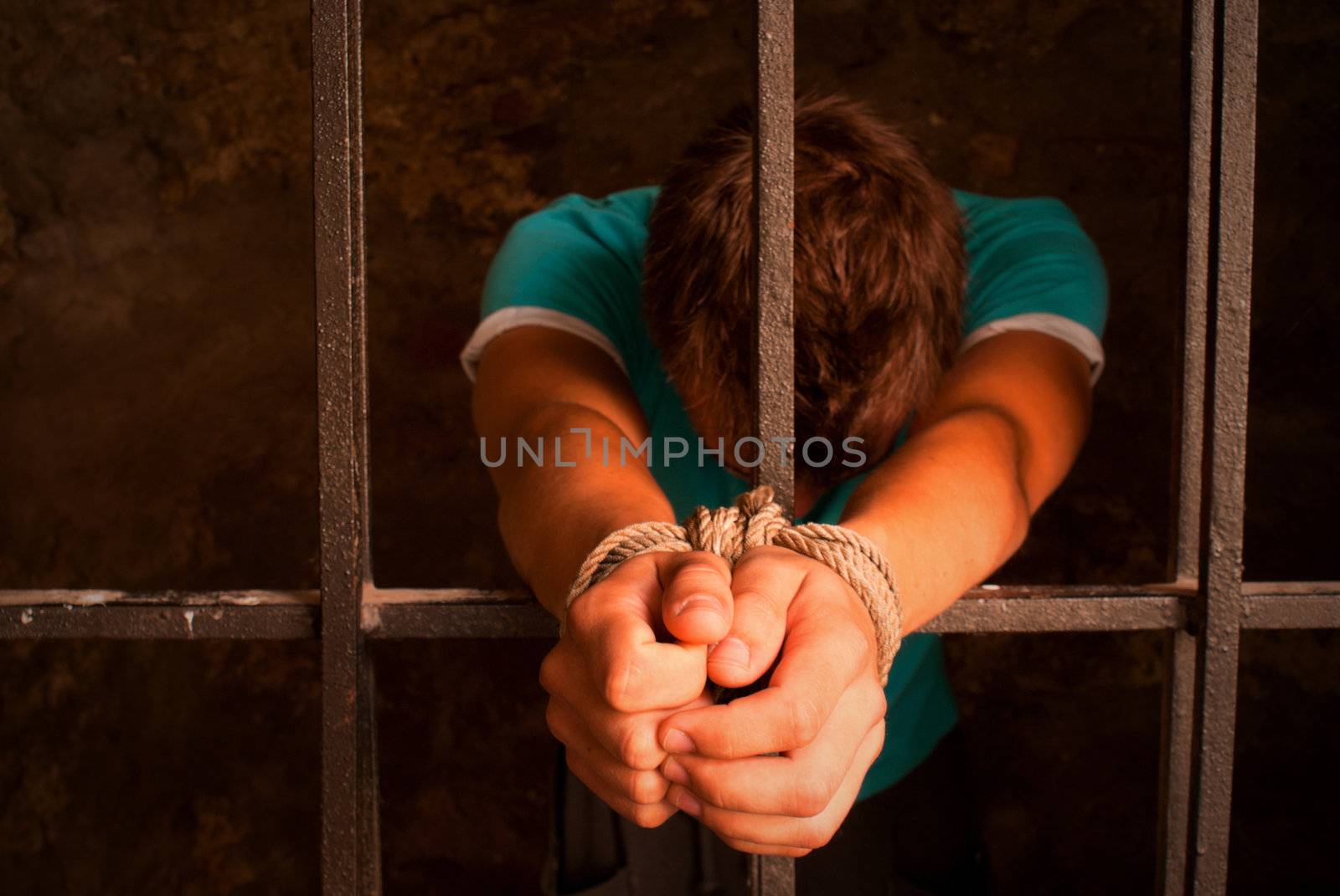 Man with hands tied with rope behind the bars