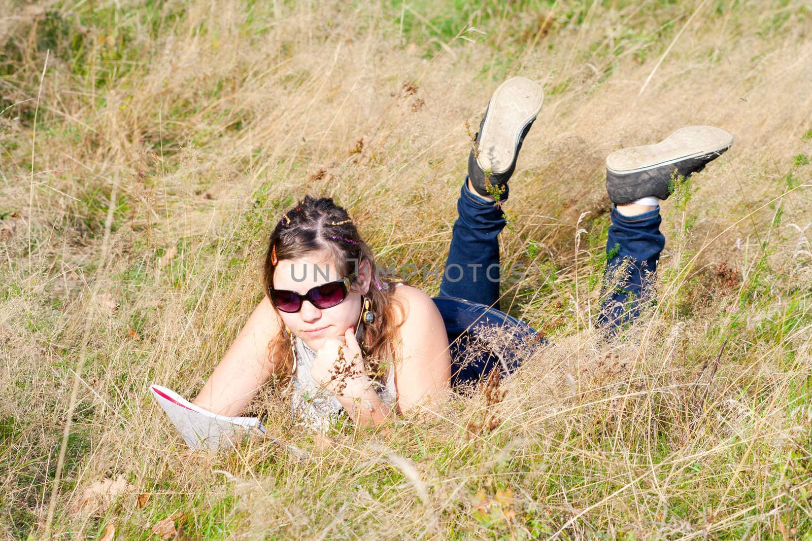 A girl who is studying in nature. It lies on the sunny meadow by the woods, reading.