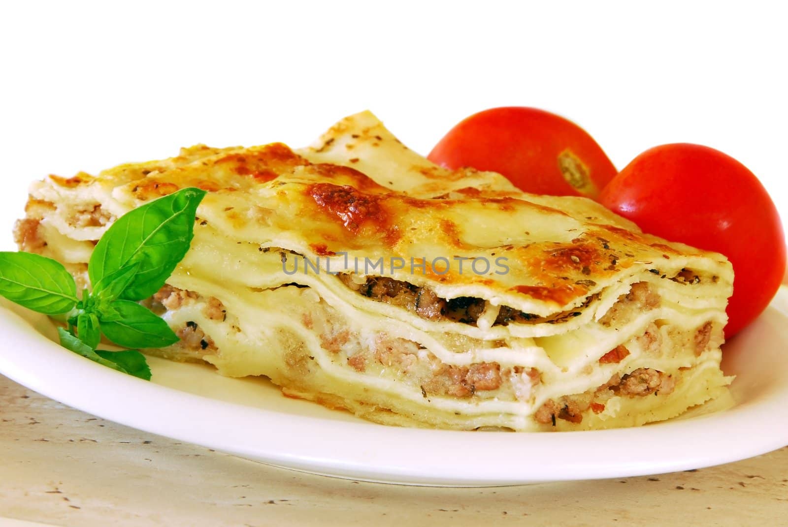 appetizing lasagna piece with basil and tomatoes on white plate