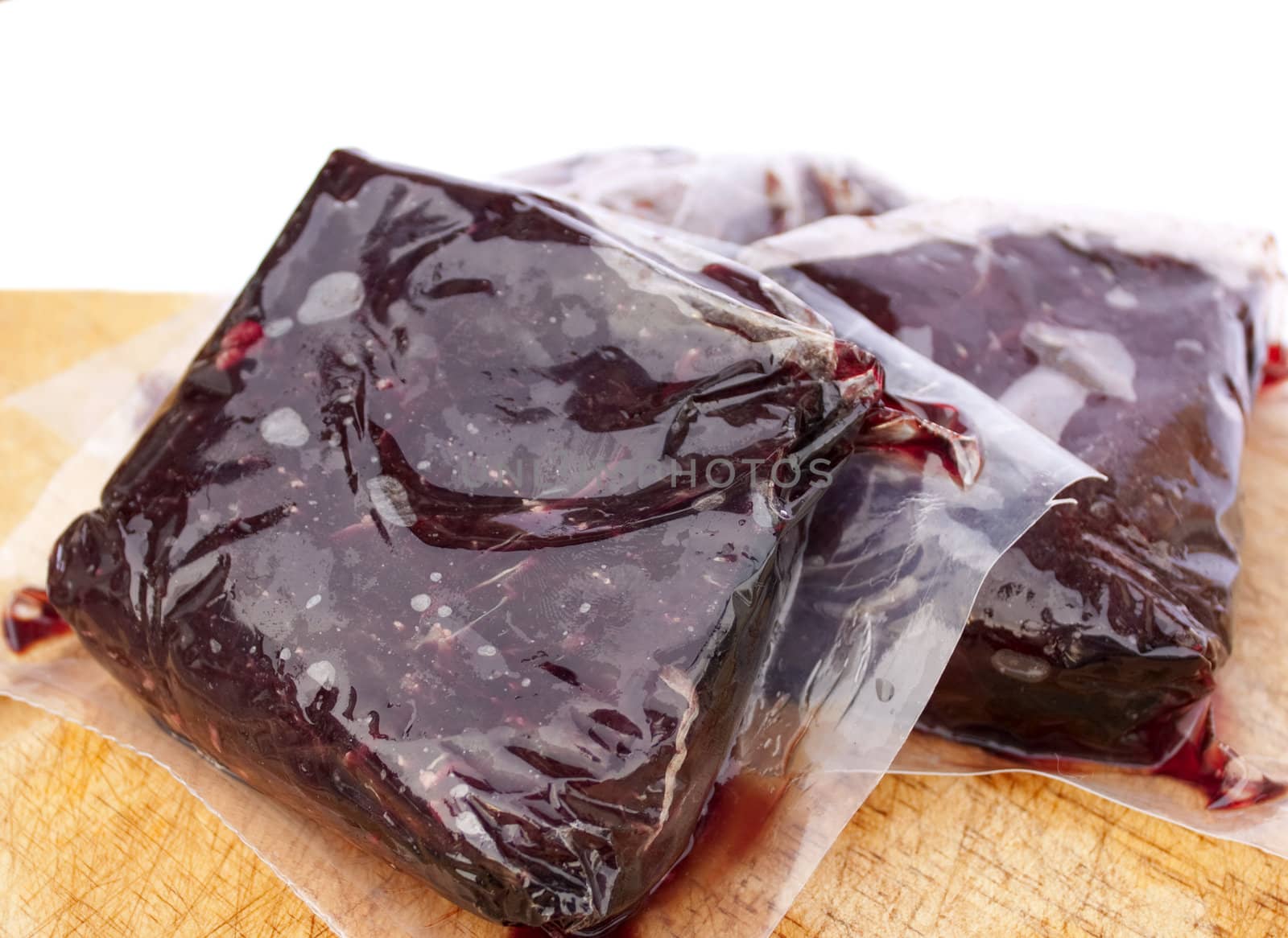 Vacuum sealed whale meat on a wooden board with white background.