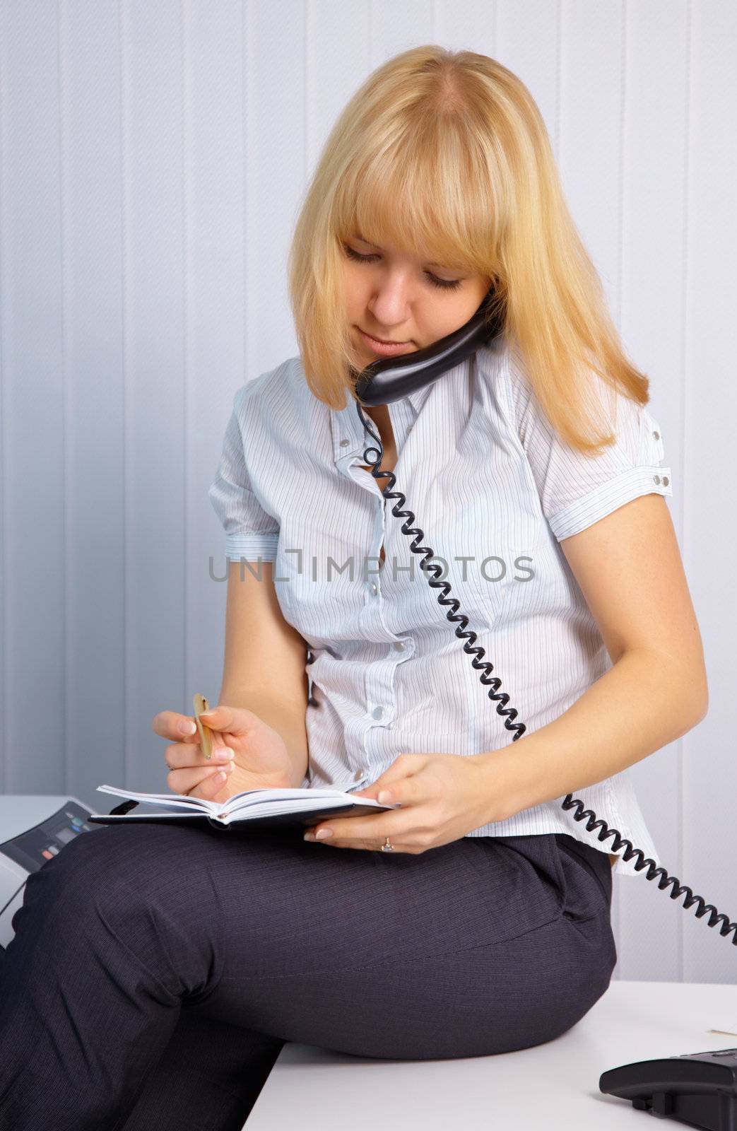 Young secretary takes calls while sitting on the table