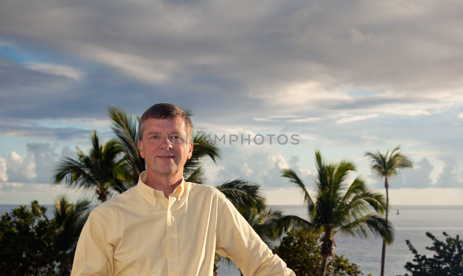 Retired man smiling as the sun sets behind over the palm lined ocean