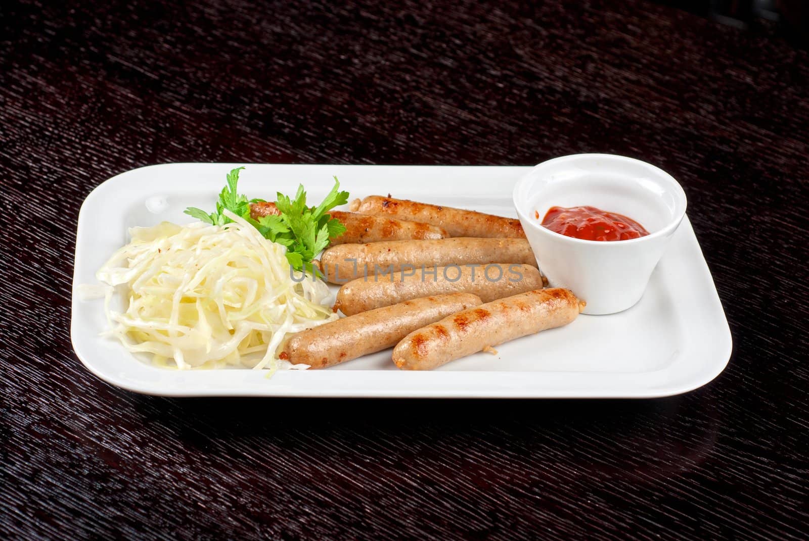 Grilled sausages with cabbage, greens and tomato sauce on white plate