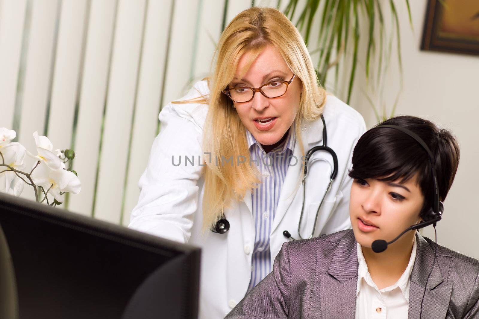 Female Doctor Discusses Work on Computer with Receptionist Assistant in An Office Setting.
