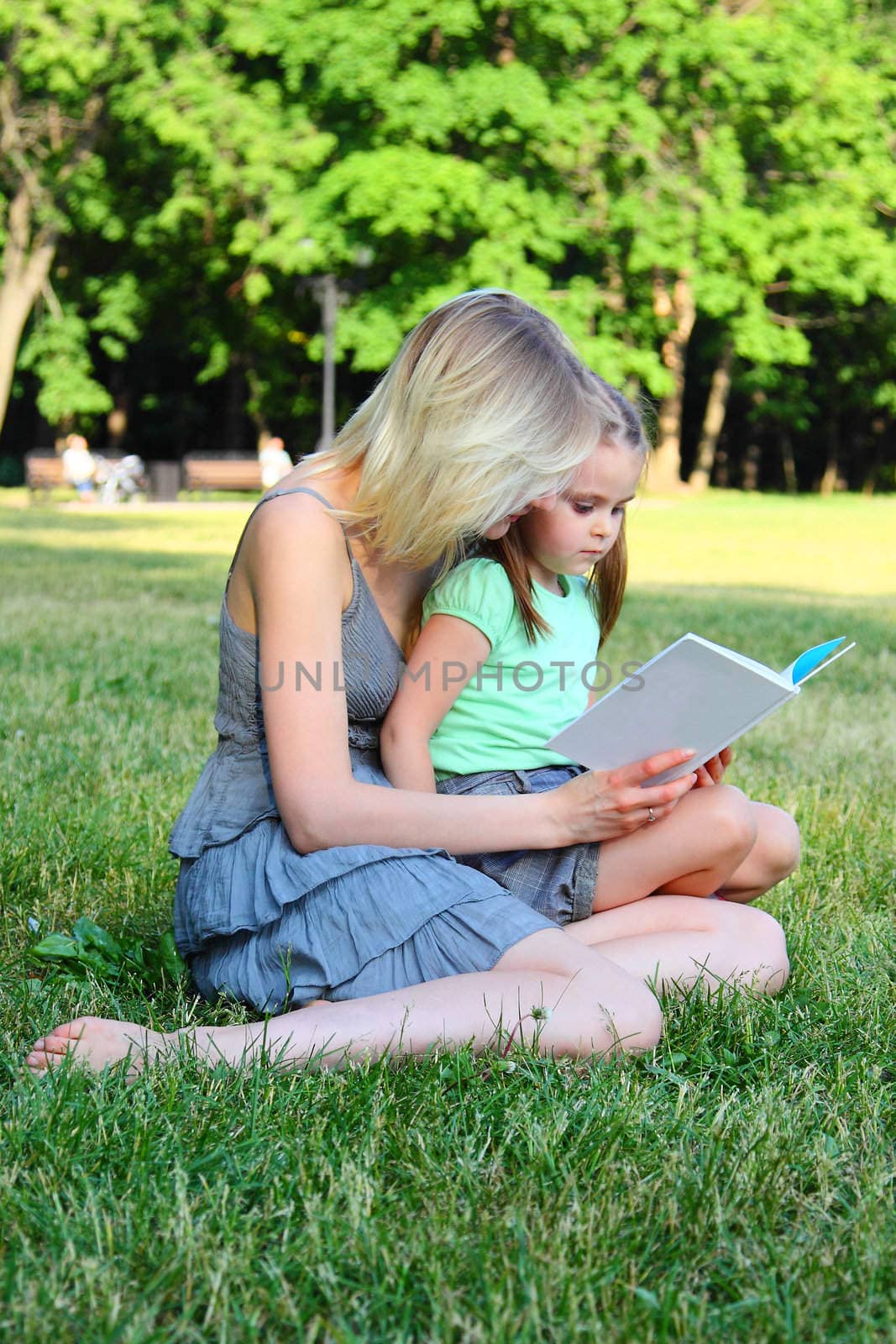 Young mum reads to the children the book during walk in park
