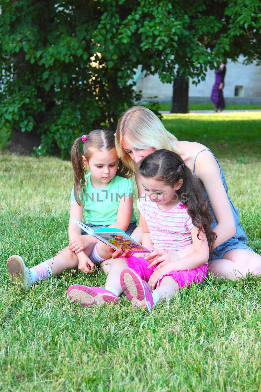 Young mum reads to the children the book during walk in park