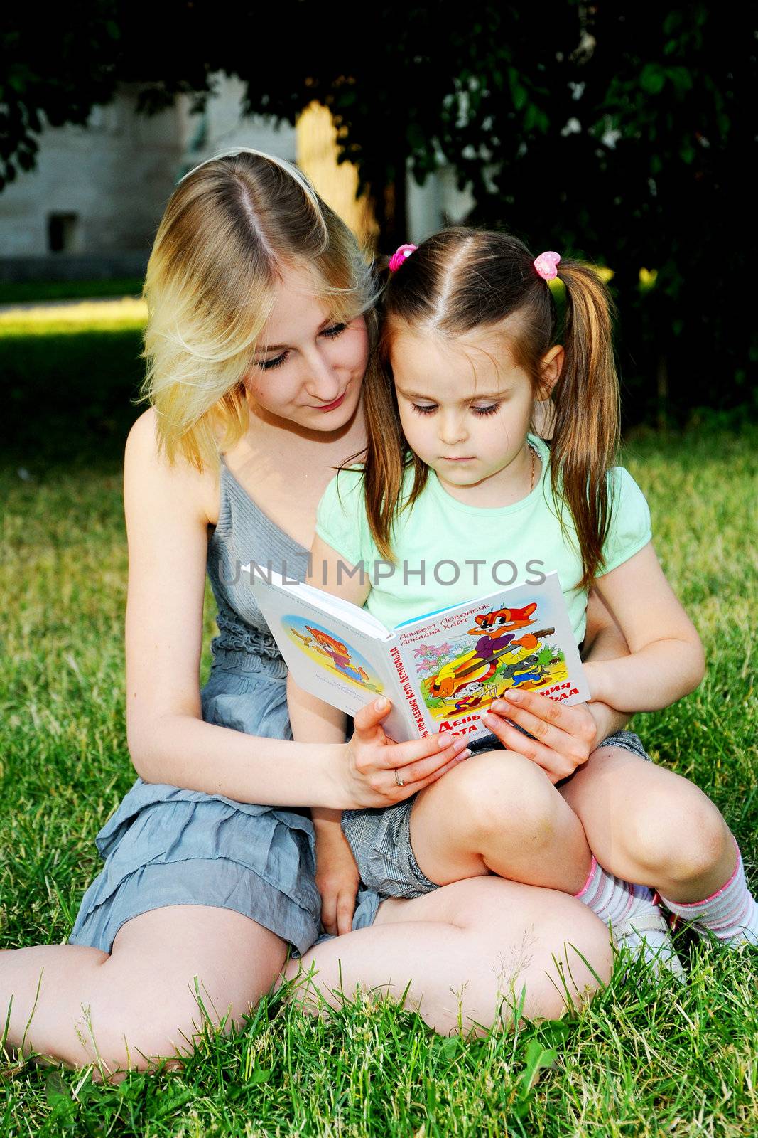 Young mum reads to the children the book during walk in park