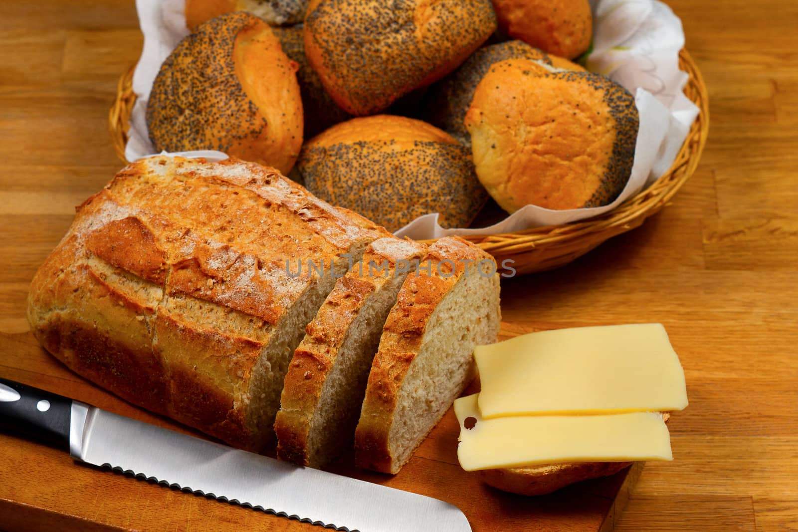 Fresh bread cheese and knife on wooden cutting board with basket with bread rolls in the background