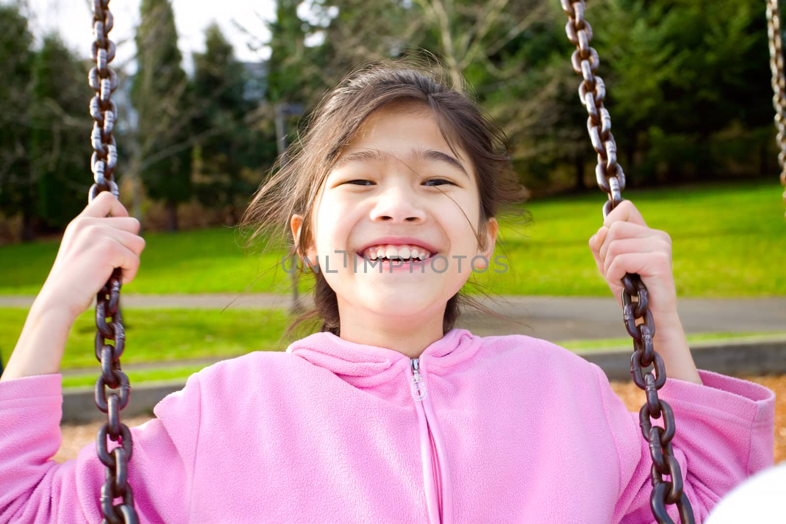 Happy little nine year old part Asian girl smiling on a swing at the park